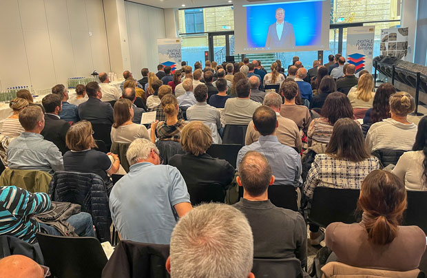 Blick von hinten auf einen vollbesetzten Vortragssaal. Vor dem Publikum eine Leinwand mit Bauminister Christian Bernreiter.